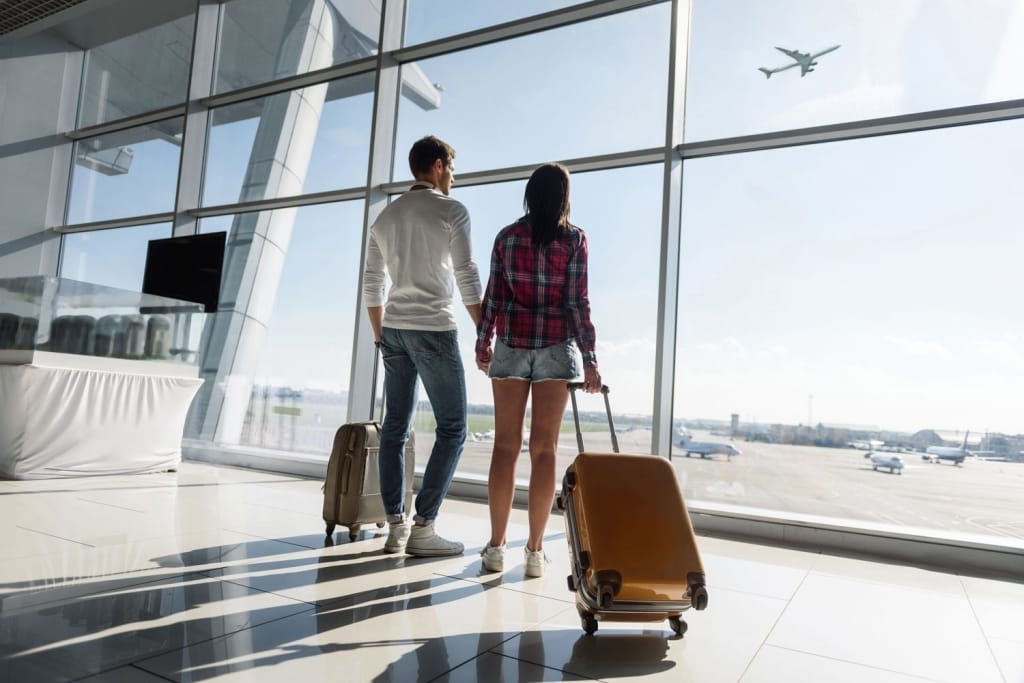 Young man and woman are looking through window at airport