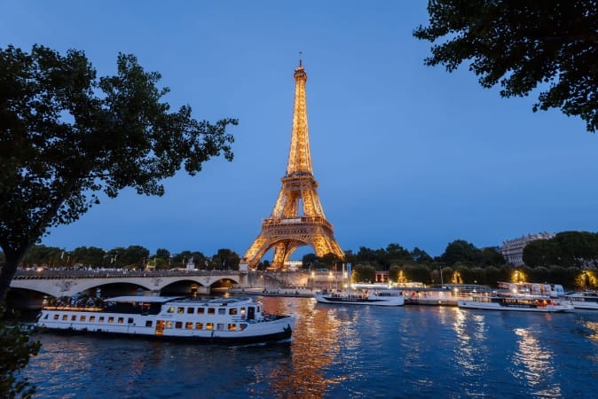 Eiffel Tower, cruise boats and bridge on Seine river at night in Paris, France