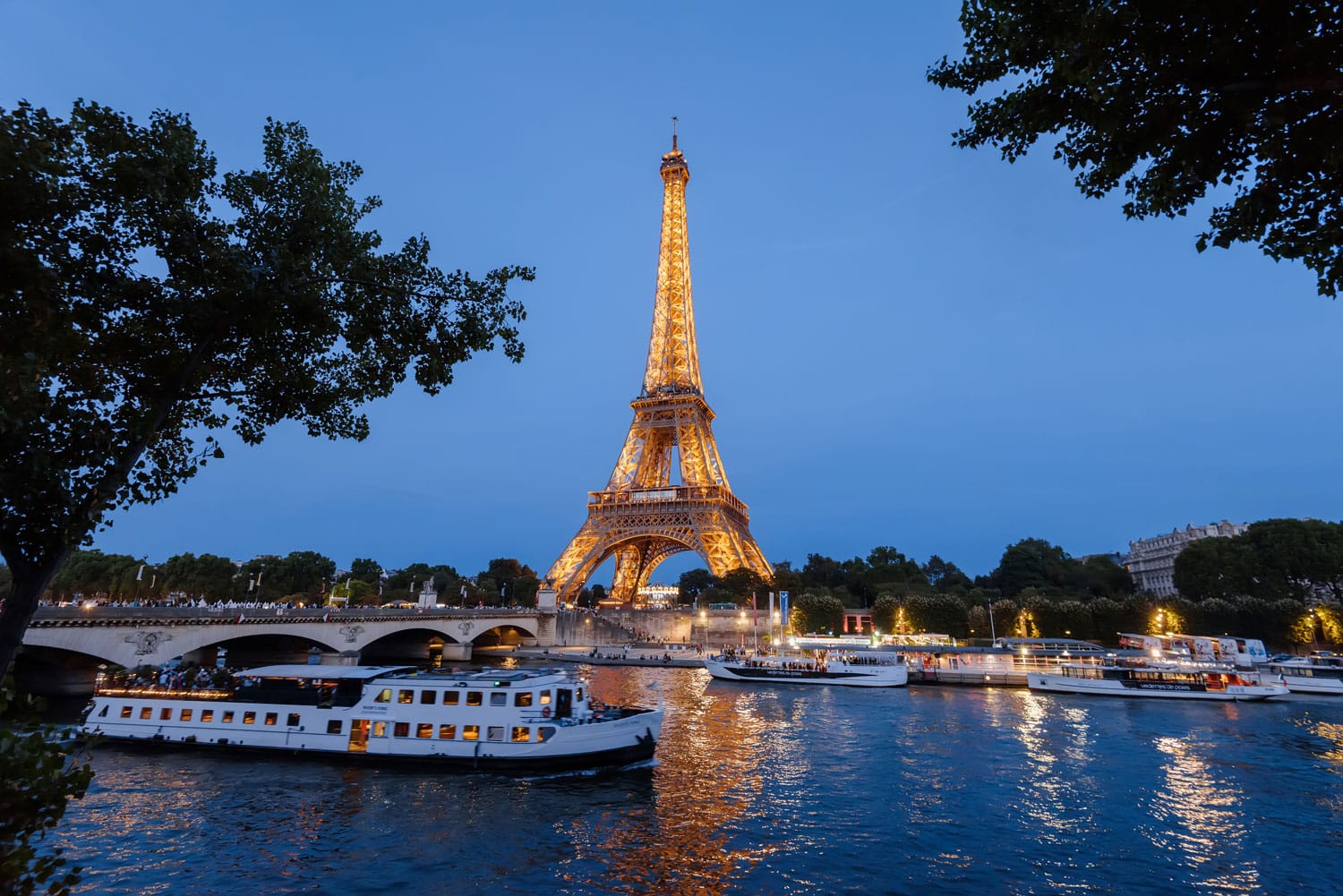 Eiffel Tower, cruise boats and bridge on Seine river at night in Paris, France