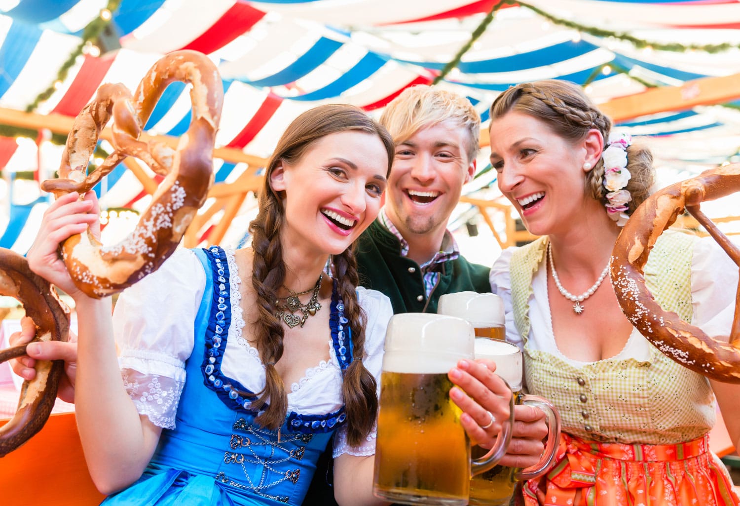 Three friends in beer tent at Dult or Oktoberfest holding giant pretzels up in the air