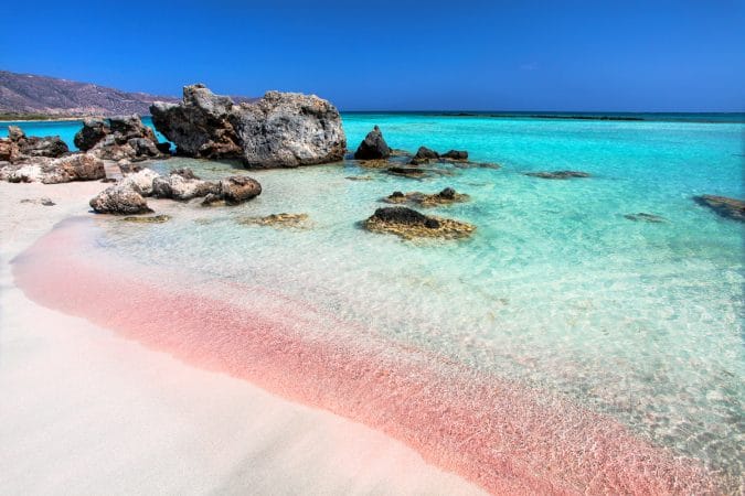 The wave of the sea on the pink sand and beautiful beach with cliffs. Coast of Crete island in Greece. Pink sand beach of famous Elafonisi (or Elafonissi).
