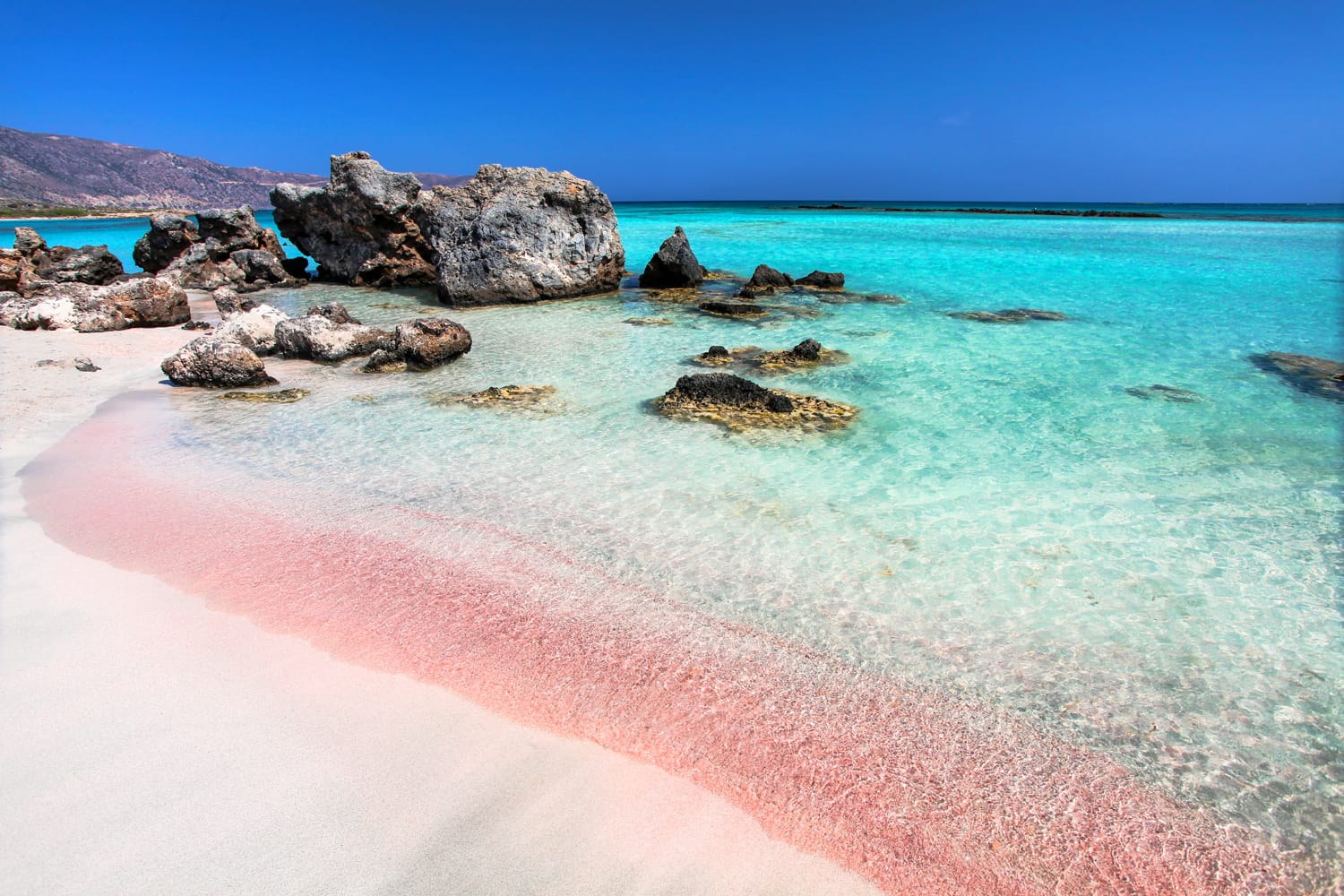 The wave of the sea on the pink sand and beautiful beach with cliffs. Coast of Crete island in Greece. Pink sand beach of famous Elafonisi (or Elafonissi).