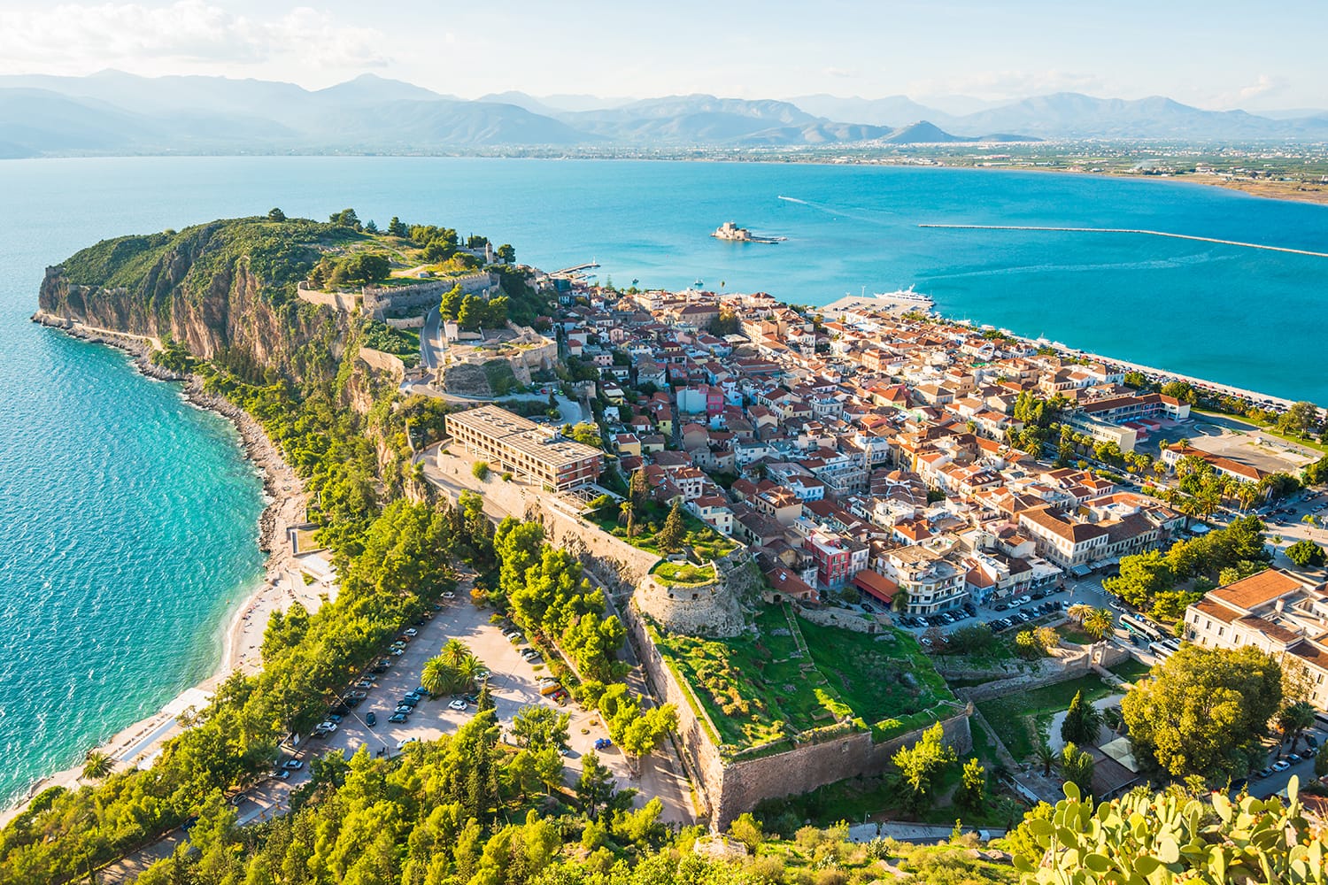 Green peninsula with Nafplion city in Greece from above with blue Mediterranean sea, old town roofs and small port