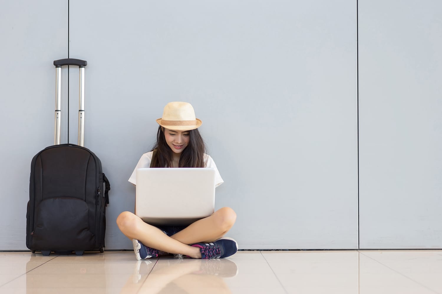 Asian woman teenager using laptop computer at airport terminal sitting with luggage suitcase and backpack for travel in vacation summer relaxing waiting flight transport or booking ticket