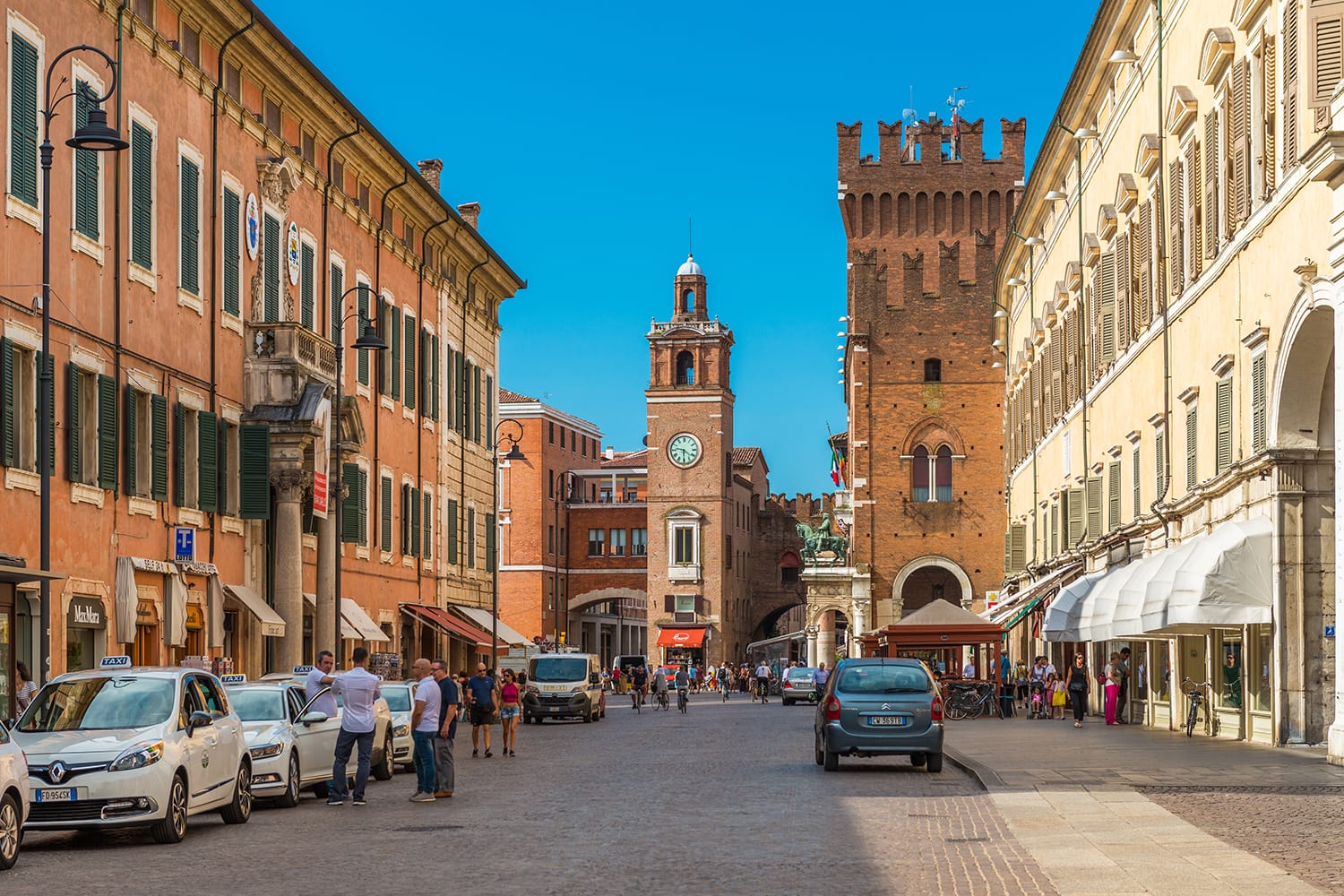 Central street of Ferrara. Taxi cabs and drivers near them. People walking in the historical part of the city