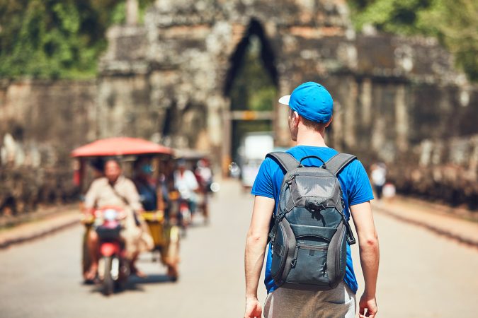 ourist in the ancient city. Young man with backpack coming to ancient monuments. Siem Reap, Cambodia