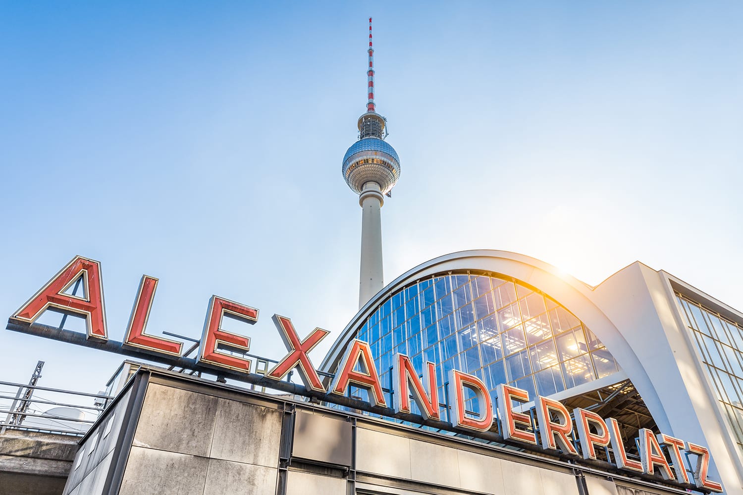 Wide-angle view of Alexanderplatz neon sign with famous TV tower and train station in golden evening light at sunset in summer, central Berlin Mitte district, Germany