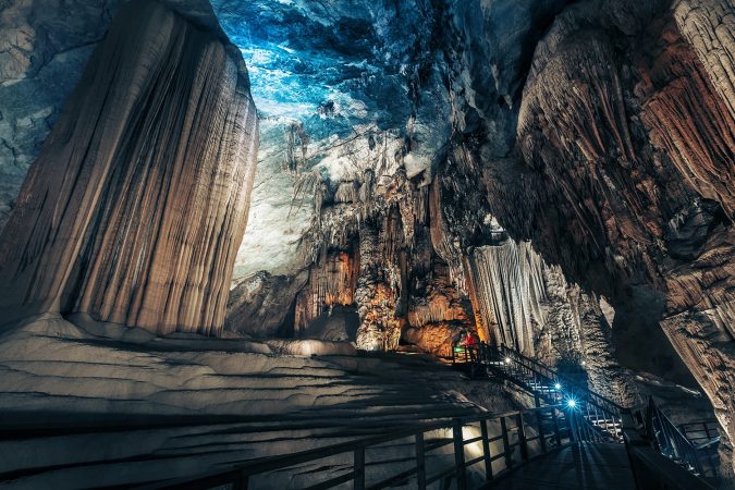 Tourist in red jacket standing in the huge illuminated cave in the region of Phong Nha National Park, Vietnam