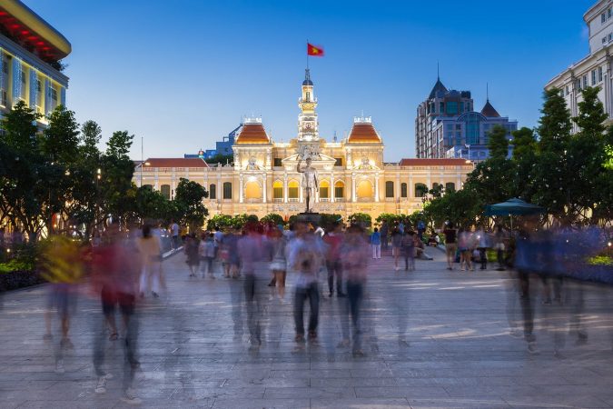 People are walking and taking pictures in front of the City Hall building, Ho Chi Minh City, Vietnam.