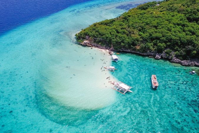 Aerial view of sandy beach with tourists swimming in beautiful clear sea water of the Sumilon island beach landing near Oslob, Cebu, Philippines