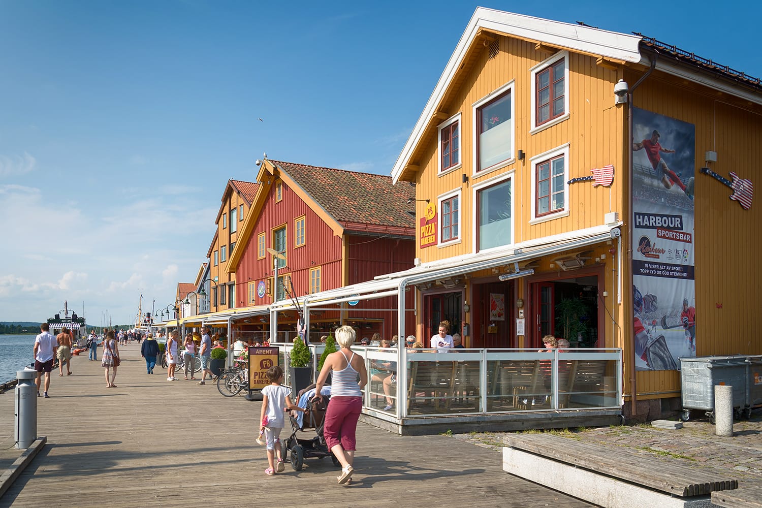 People enjoying the summer sunshine beside the al fresco restaurants and modern apartment buildings of Tonsberg town, Norway
