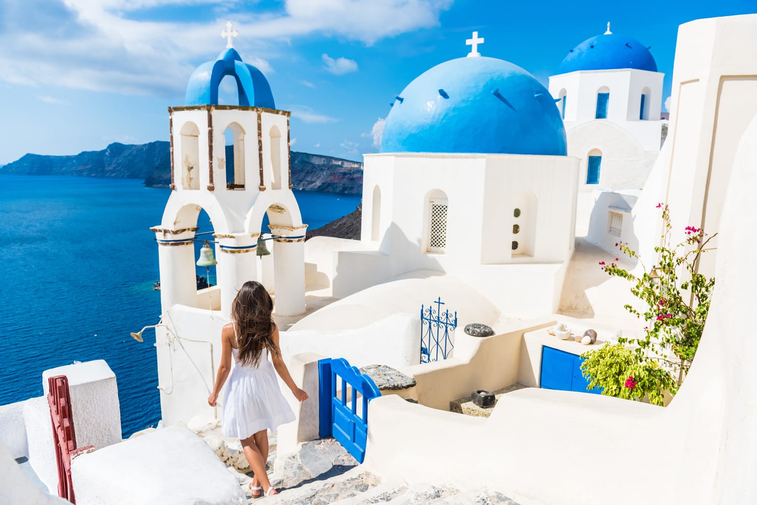 Santorini travel tourist woman on vacation in Oia walking on stairs. Person in white dress visiting the famous white village with the mediterranean sea and blue domes.