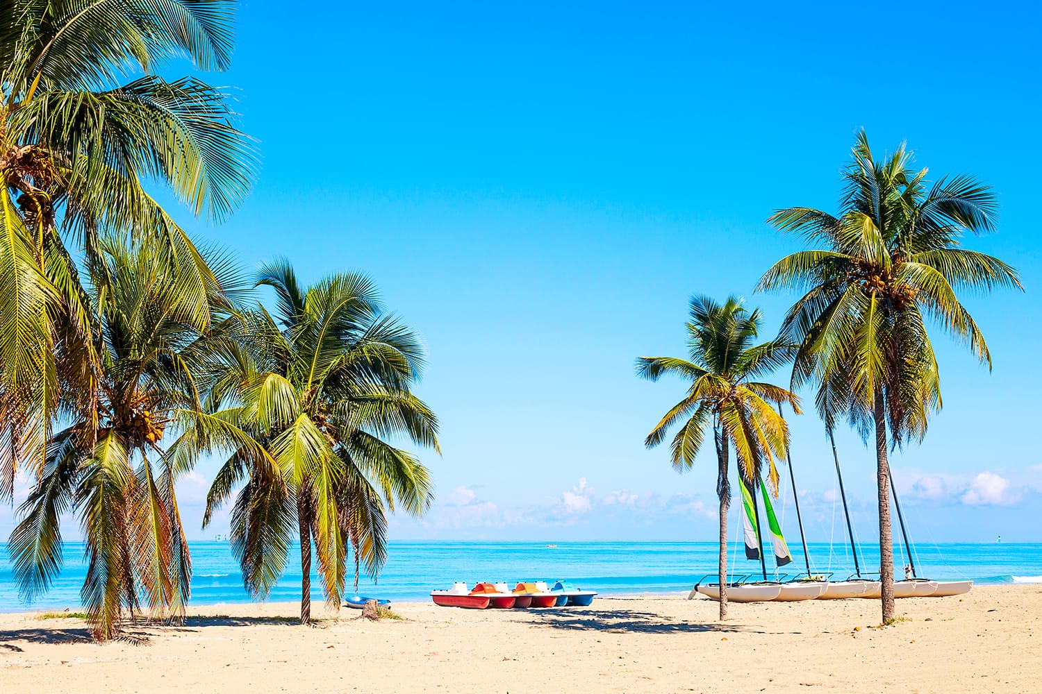 The tropical beach of Varadero in Cuba with sailboats and palm trees on a summer day with turquoise water.