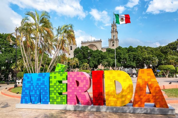 Colorful Merida sign with a Mexican flag and cathedral in the background in Merida, Mexico