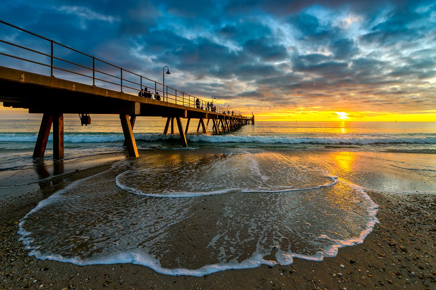 People walking along Glenelg Beach jetty at sunset, South Australia
