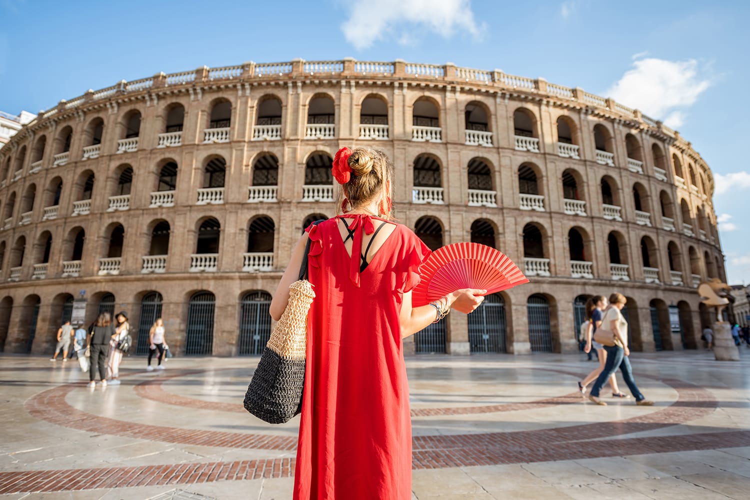 Woman in red dress with spanish hand fan stnading back in front of the bullring amphitheatre in Valencia city, Spain