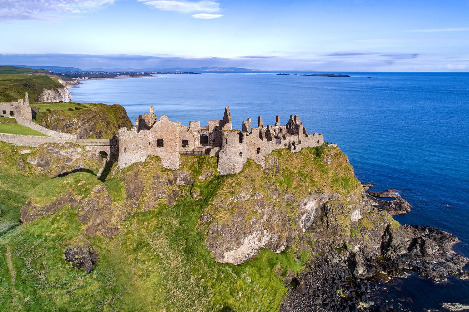 Ruins of medieval Dunluce Castle, cliffs, bays and peninsulas. Northern coast of County Antrim, Northern Ireland, UK. Aerial view.