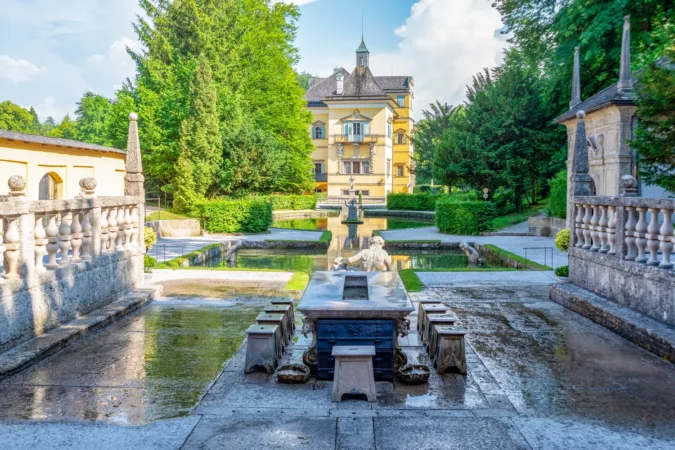 Trick fountains hidden in a dinner table and sculptures at the pond in Public Gardens of Hellbrunn Palace (Schloss Hellbrunn) in Salzburg