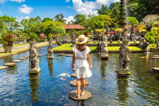 Woman traveler wearing white dress and straw hat at Taman Tirta gangga temple on Bali, Indonesia