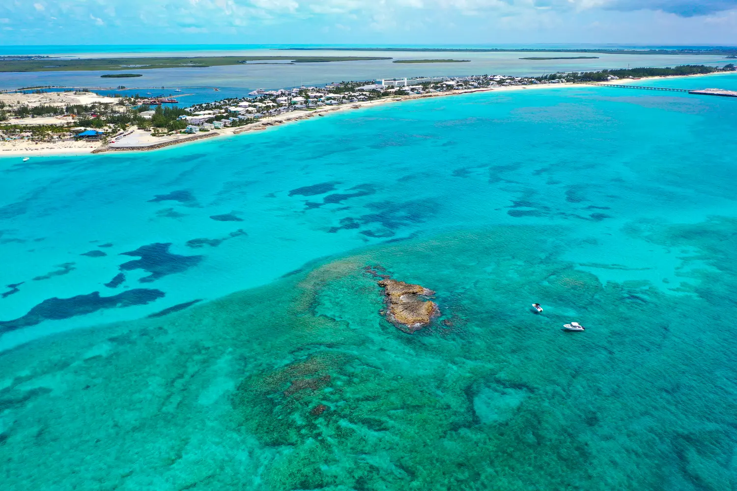 Aerial view of boats anchored off coral rocks with North Bimini, Bahamas in the background.